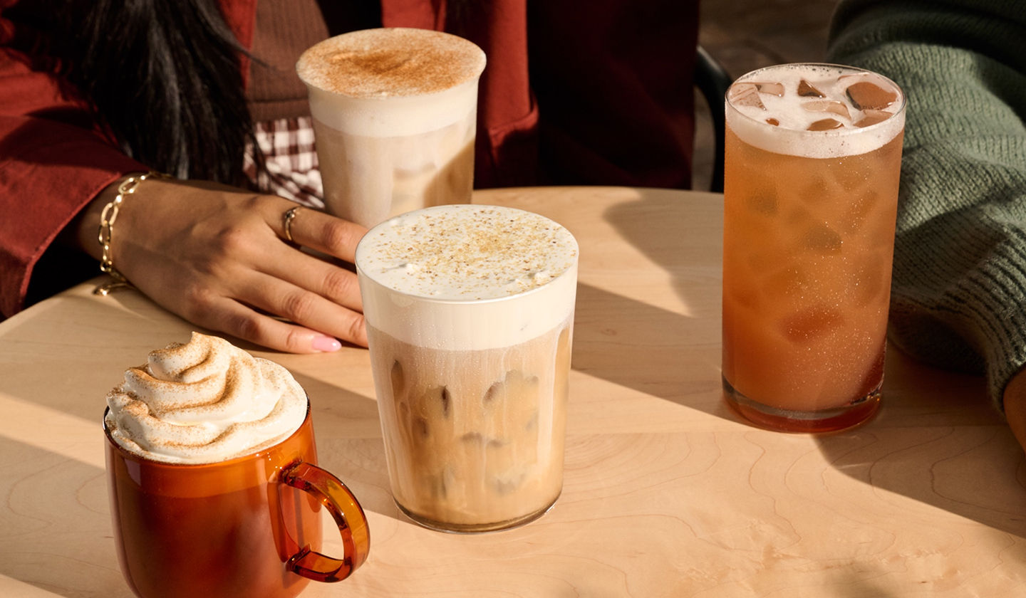 Quatre boissons d’automne posées sur une table autour de laquelle des personnes sont rassemblées.